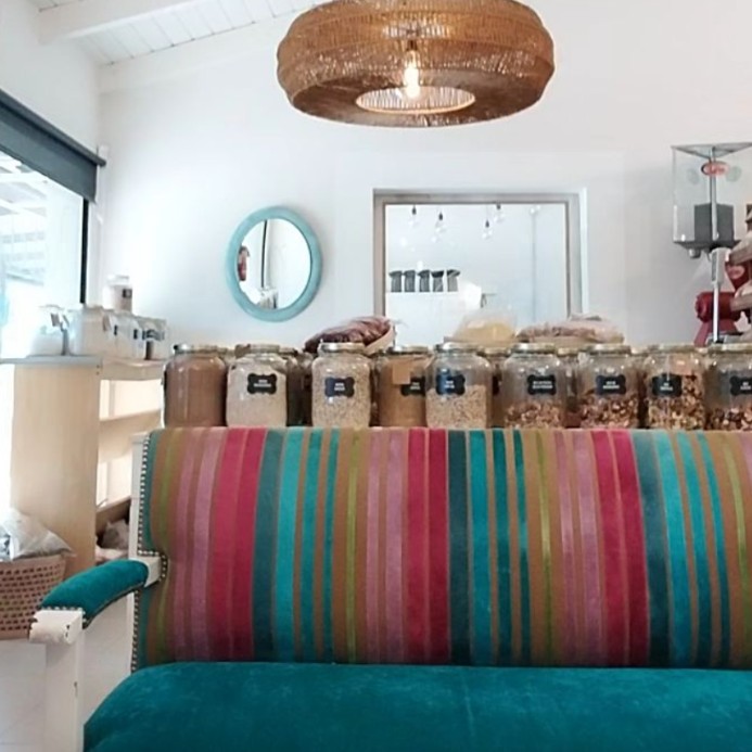Interior del local: frascos a granel, lámpara de mimbre y banco de colores